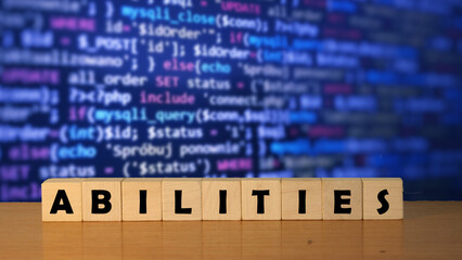 Handwritten word 'ABILITIES' displayed on wooden blocks against a blurred background of programming...