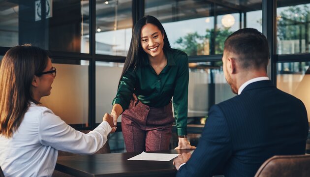 Smiling young Asian businesswoman shaking hands with a female executive at a professional boardroom meeting, concept for partnership success, recruitment welcome and closing a business deal