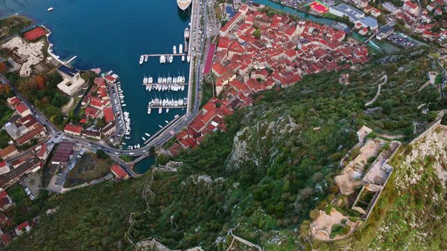 Aerial drone view of the famous zig zag hiking path leading to the fortress, next to the red roofs of Kotor Old Town and the marina