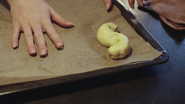 Hands of female baker working and placing dough of s-shaped yellow pastries, traditional Scandinavian holiday bakery desaturated footage easily color matched