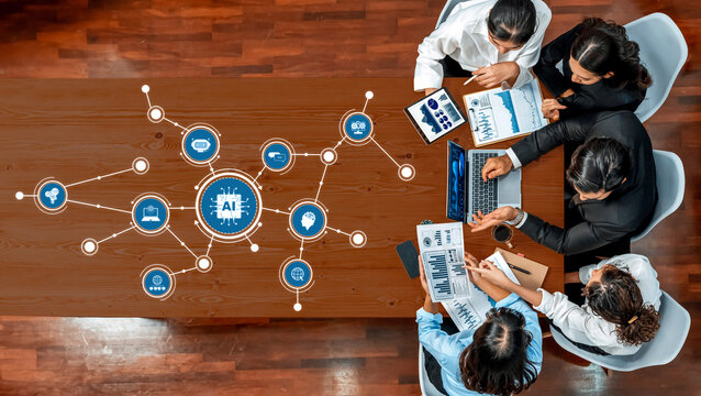 A diverse team collaborates in a bright conference room, utilizing laptops and tablets to explore artificial intelligence trends through visual data and charts. Amity - Powered by Adobe