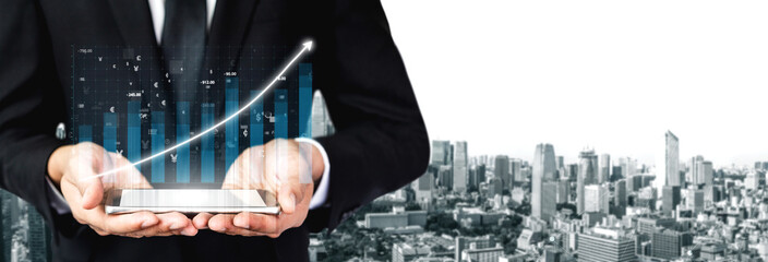 A businessman in formal attire holds a tablet displaying a financial graph. The urban skyline in the background represents modern business growth and success. Impute