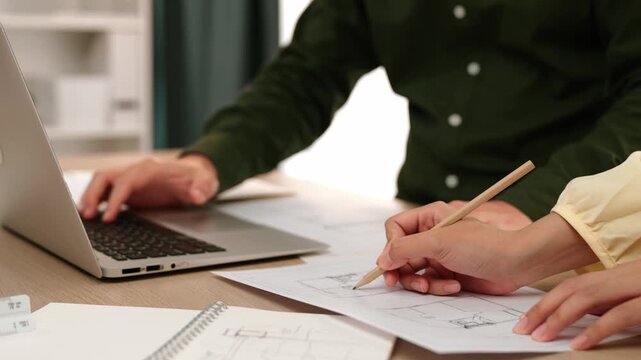 Architect and engineer compare hand writing draft with construction blueprint detail display in laptop for accurate design, measurement tool and plan on table at modern office. Closeup. Delineation.