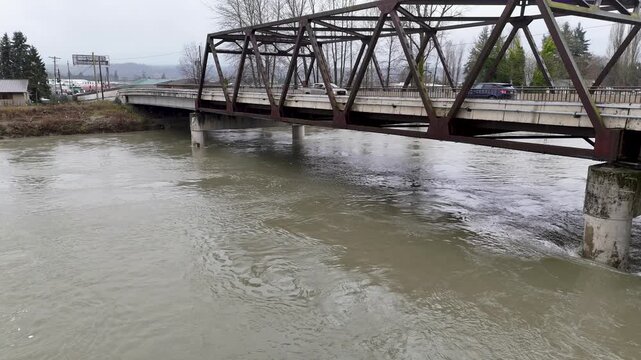 The Snohomish river in Washington state is at elevated levels due to flood water. Cars and vehicles drive over the river on a bridge. 