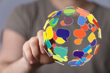 Abstract image of a hand interacting with a sphere formed of colorful speech bubbles. Concept of communication, social media, global conversatio