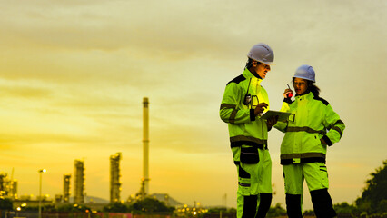 Energy professionals plan for the future at a refinery. The diverse team uses technology to monitor sustainable operations during a beautiful golden sunset.