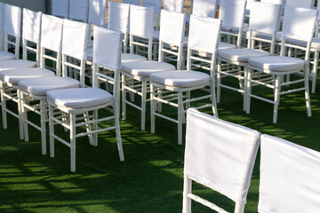 Outdoor rows of white Chiavari chairs with clean back covers on green lawn, sunlit and empty. Blank fabric ready for branding or text, ideal seating mockup for conference, wedding or event