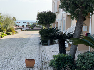 A serene pathway between charming beachfront cottages leads to the sandy shore, offering a peaceful view of the ocean and an invitation to relax.
