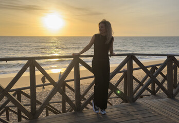 A wooden boardwalk overlooking the ocean. The boardwalk is empty and the sky is blue. The sun is setting and the water is calm © Angelov