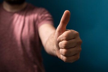 Close-up of a man's hand giving thumbs up gesture on a blue background. Perfect for concepts like positive, okay