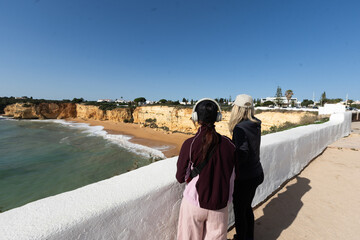 A mother and daughter enjoying the beautiful view Yellow rocks and cliffs on the sandy beach. A cove by the sea, Our Lady of the Rock, Praia Nova, Lagos. Algarve, Portugal