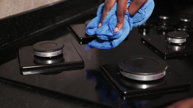Close-up, hands of young African woman cleaning a modern kitchen stovetop with a microfibre cloth, domestic care and everyday chores