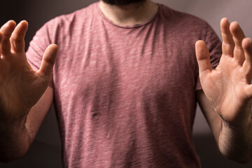 Close up of a man with open hands in a protective gesture, blocking or rejecting something. Wearing a t-shirt, c