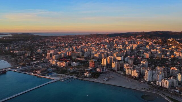 Aerial drone view of Vlora, Albania, showcasing the city's dense coastal skyline, mountain backdrop, and turquoise seafront