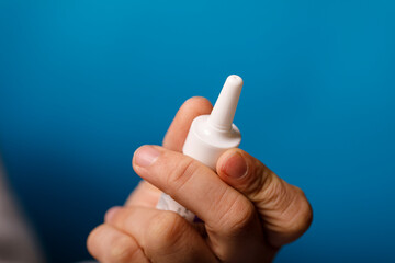 Close-up of a hand holding a white nasal spray bottle against a bright blue background. Ideal for health, alle