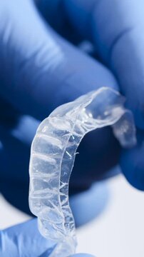 Clear dental aligner being held in gloved hands for examination and demonstration at a clinic