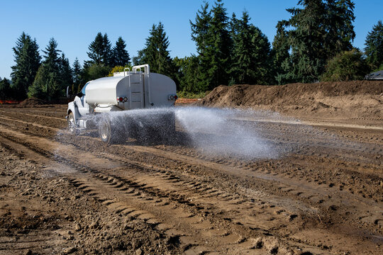 New residential housing development construction site, non-potable water truck spraying water to keep dust down during earthworks project, sunny fall day 
