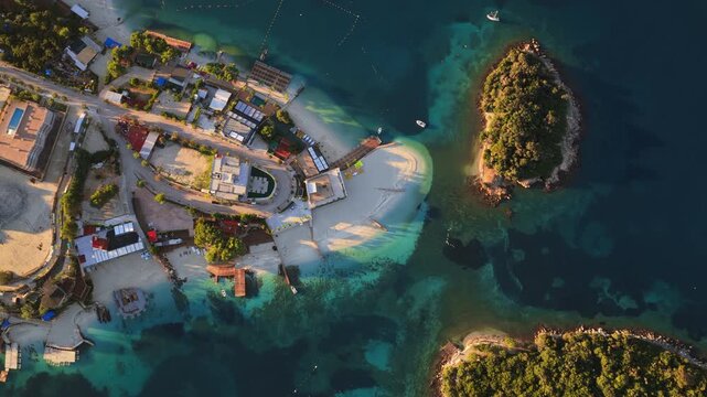 Aerial drone view of Ksamil town, it's dense cluster of hotels and houses, and the iconic bright blue bays with floating platforms and beach clubs