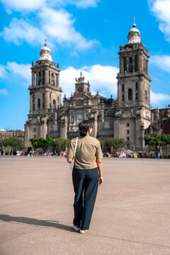 Unrecognized Latin woman standing calmly at Metropolitan Cathedral in Mexico City&rsquo;s Zocalo during a bright sunny, wearing casual urban clothes, surrounded by open space and historical buildings