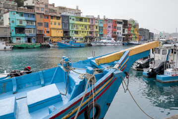 Zhengbin Fishing Port, The vibrant colorful houses serve as a scenic background to a traditional blue fishing boat docked at the pier in Keelung, Taiwan.