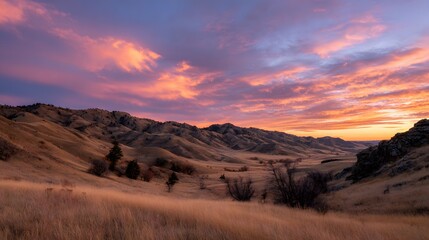 Naklejka premium Dramatic Sunset Over Rolling Hills Landscape with Golden Grass.