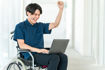 A young Asian man in a wheelchair using a computer (fist pump, hard work, success)