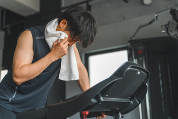 Young Asian man doing aerobic exercise on a walking machine in a sports gym