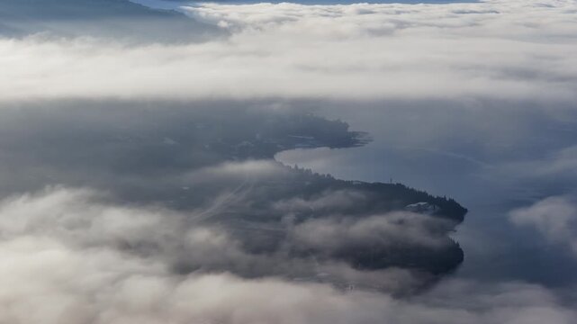 Aerial drone view of Ohrid city partially obscured by drifting fog, with the marina and waterfront emerging from the mist while the mountains loom in the distance.