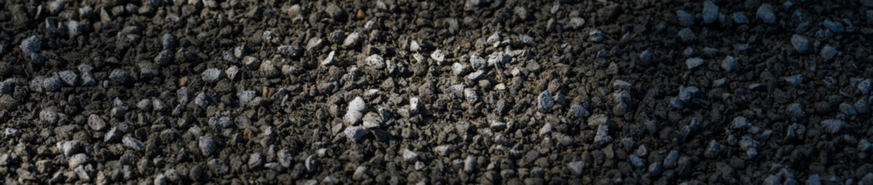 Freshly laid and raked gravel on a public park woodland path, sun and shadows, as a background
