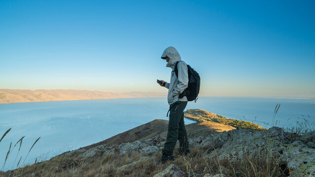 A hiker checking navigation on smartphone while standing on a rocky slope above Lake Sevan, Armenia, during an early morning hike.