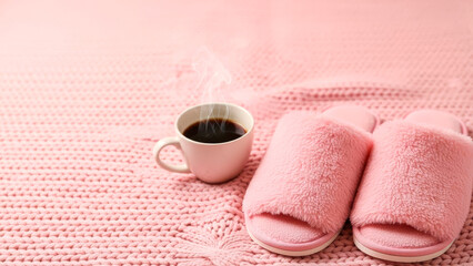 Steaming coffee mug with cozy pink slippers on knit blanket