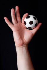 Fototapeta premium Open hand showing a small soccer ball on a black background, symbolizing mental balance and passion for sports