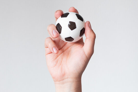 Hand lifting a small soccer ball on a neutral background, concept of healthy habits and sports therapy