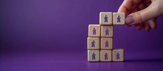 Hand placing a wooden block with a person icon onto a stacked tower of wooden blocks with human silhouettes on a purple background, conveying careful team building and selection