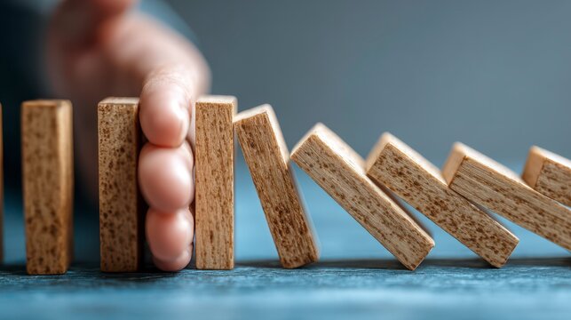 Close-up of hand preventing the domino effect. Series of wooden blocks falling one another in an illustrative concept
