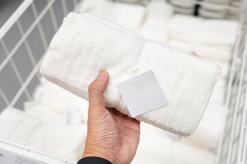 Hand Holding White Folded Towel with Blank Label in Retail Store. shopping, home essentials, hotel supplies, spa products, branding, and product mockups.