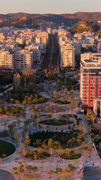 Aerial drone view of the golden hour lighting highlighting Vlora's central urban park, featuring circular pathways, palm trees, playgrounds, and landscaped green spaces. Durres, Albania, Vertical