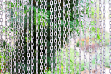 Gray iron chain curtain hanging on green garden background