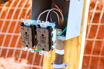 Electrical outlet components attached to wooden post next to fence for outdoor use