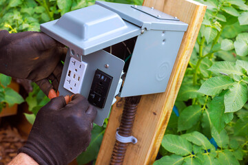 Worker installs electrical outlet in garden to enhance power access for tools equipment