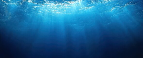 Sunlit ocean surface seen from below with shafts of light piercing deep blue water, creating a calm and serene underwater atmosphere