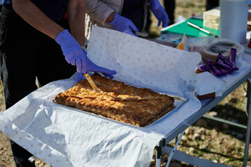 Outdoor Food Prep: People Wearing Gloves Cutting Fresh Baked Pie On Table At A Community Event
