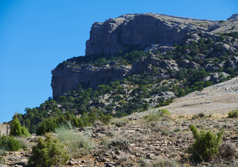 Rocky Mountain Cliff Overlook With Sparse Desert Vegetation Under Clear Blue Sky