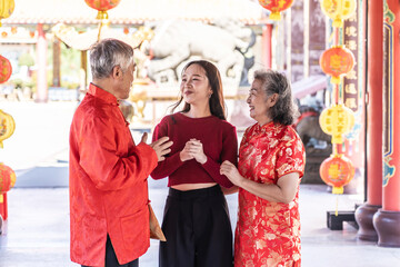 Obraz premium Portrait of asian father, mother, and their teenage daughter share laughter and happiness while talking at a vibrant Chinese temple adorned with lanterns, capturing a perfect family moment.