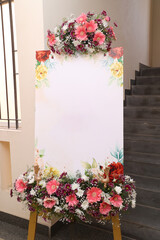 an empty invite banner decorated with colorful flowers in front of a wedding banquet hall