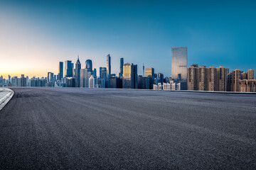 Naklejka premium Empty asphalt road with a modern city skyline at dusk.