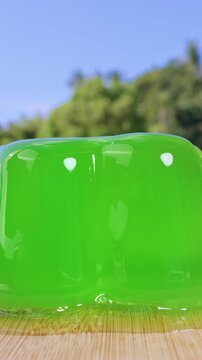 Vertical video. Close Up Shot of Green Jelly on Wooden Board Wobbling After Spoon Touch, Slow Motion Dessert Reaction with Hand Holding Spoon, Outdoor Sweet Food Impact Concept