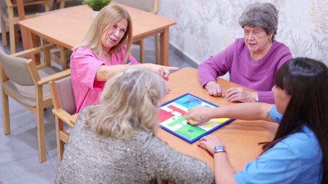 Elderly women and caregivers playing Parcheesi at nursing home