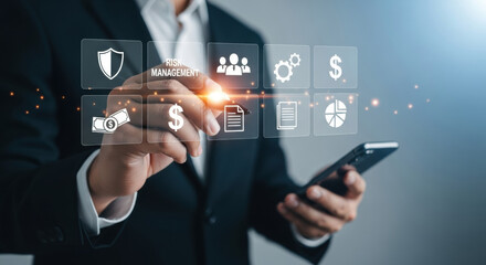 A businessman in a suit touches a futuristic digital interface displaying various business icons. Fintech concept with soft blue light and a shallow depth of field.