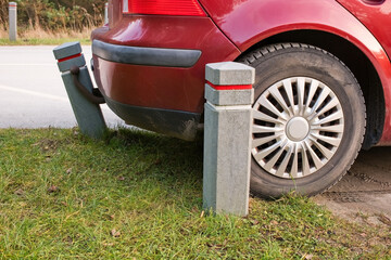 Red car parked too close to bollard on edge of parking lot, rear bumper almost touching concrete post, concept of bad parking, danger of damage and road safety.